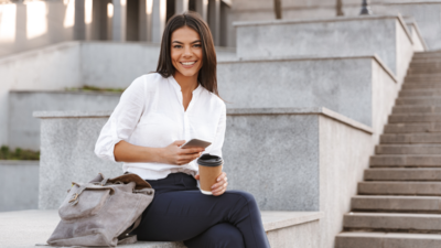 Woman sitting on steps outside holding a phone and coffee cup