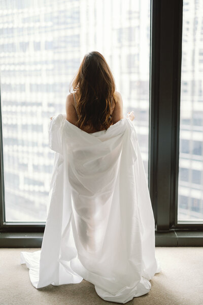 A woman poses with a sheet while looking out the window of her suite at the Langham Hotel in downtown Chicago.
