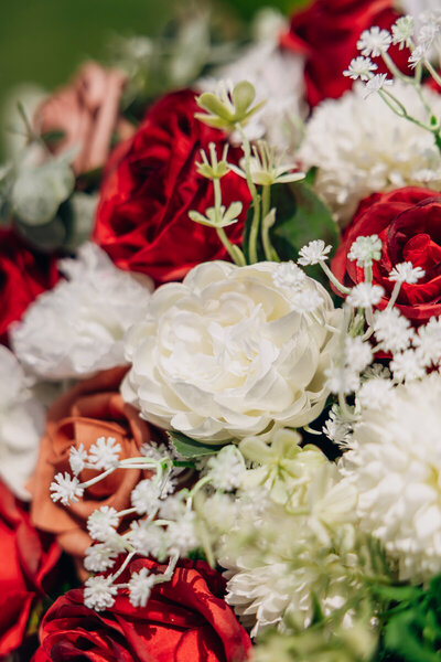 Close-up of a bridal bouquet featuring red, orange, and white flowers with baby's breath