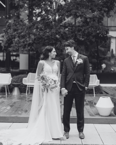 Black and white photo of bride and groom holding hands and smiling at each other