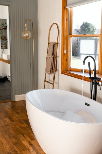 A white porcelain soaking tub in a minimal, wood accented bathroom.