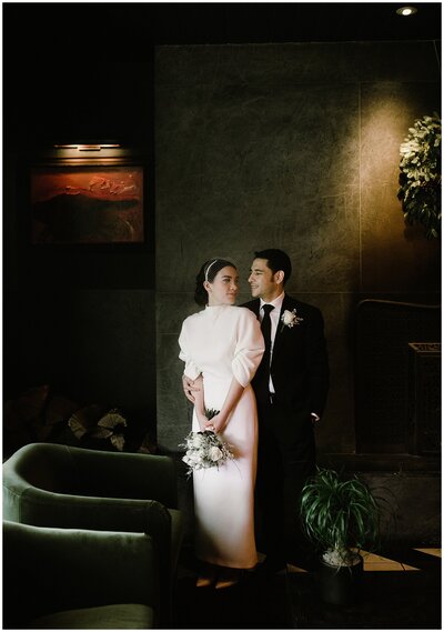 Bride wearing white dress with ruffled sleeves holding bouquet with groom in black suit standing beside her.
