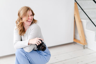 Brook kneeling down with camera, laughing while looking out of frame. 