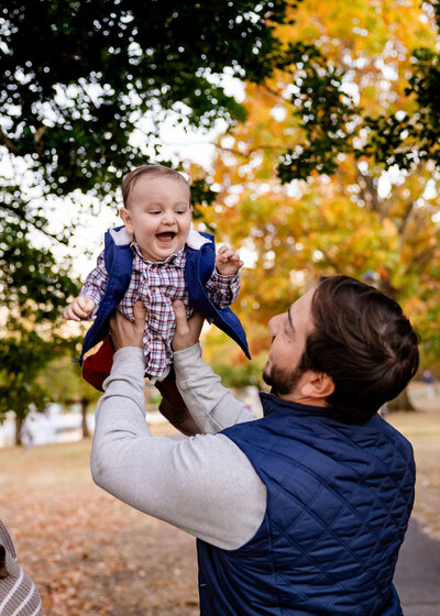 Lifestyle photo of a father holding his smiling baby in the air at an Essex County, New Jersey park.