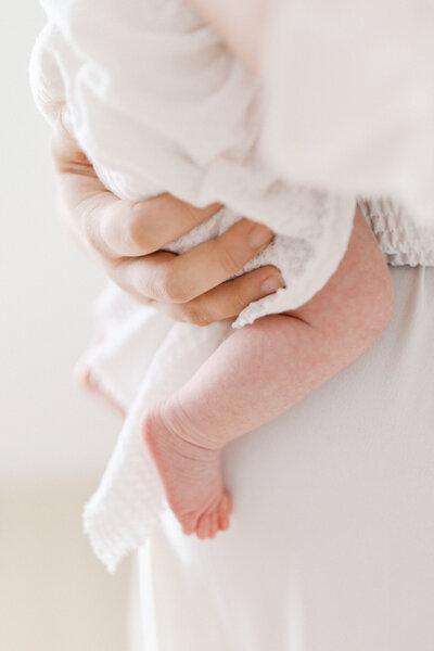 A close up photo of a baby's feet and legs while being held close to his mother.