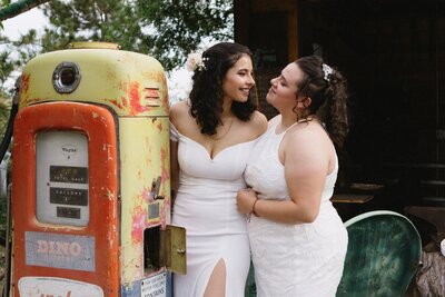 An LGBTQ+ couple gaze at each other as they pose next to an old gas pump.
