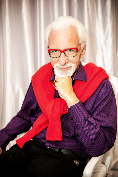 man resting his chin on his hand while wearing a purple shirt and red cardigan