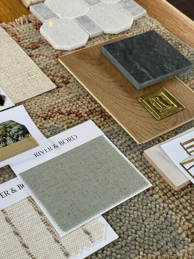Material palette flat lay with a sage and white and red area rug. White oak hardwood floors, black slate tile and white and grey marble mosaic tile. Unlaquered brass rejuvenation swatch. River & Bord sage green fabric swatch.
