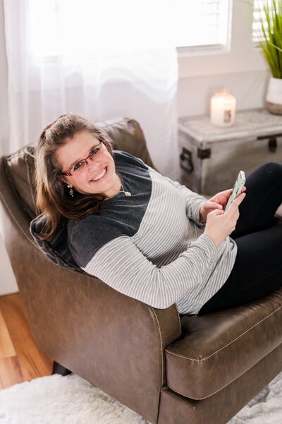 Amanda Richardson, NC brand photographer, sits back in her living  room chair answer her cell phone