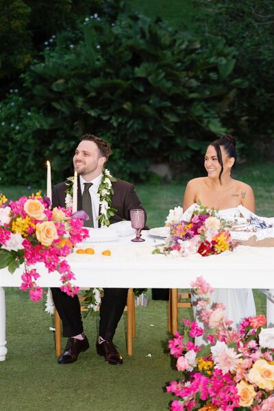 A newlywed couple sitting at a table together at their reception 
