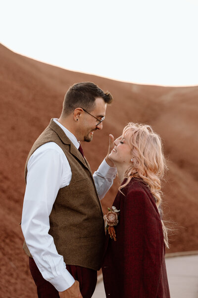 Bride wearing groom's suit jacket. They are leaning toward each other and smiling.