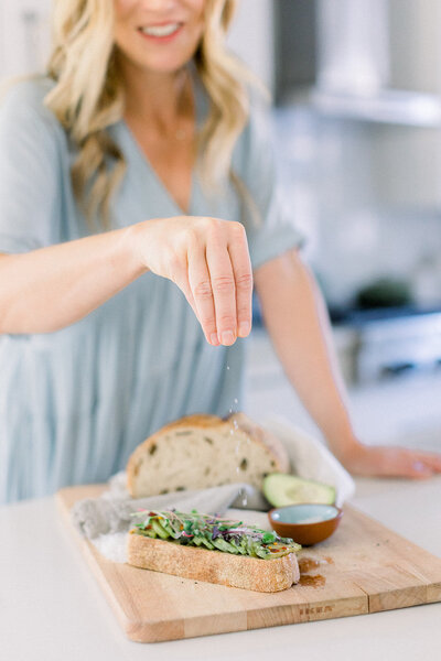 Blonde woman sprinkling salt on avocado taost