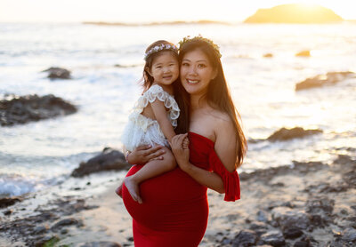 Pregnant mom in red dressed photographed with baby girl on the beach by maternity photographer Candice Berman Photography
