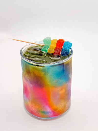 Ol’ Razzle Dazzle specialty drink from Quigley Coffee Co, colorful iced matcha served in a rainbow glass with gummy bear garnish.