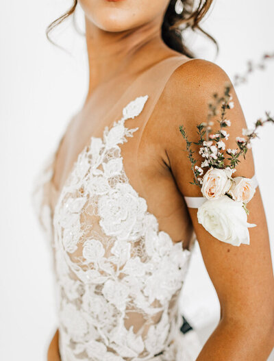 Closeup of a bride's torso wearing a lace dress and a rose corsage on her arm