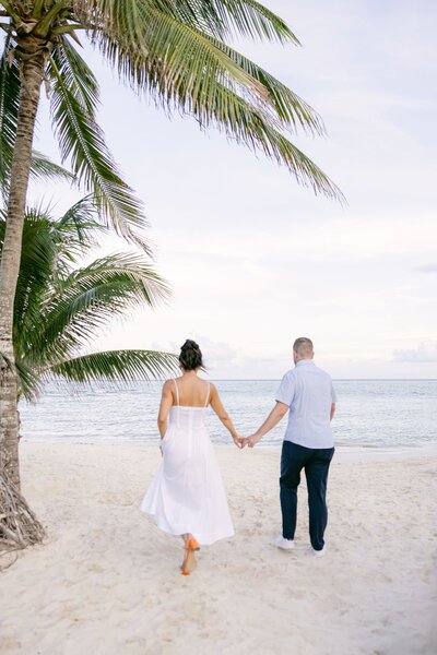 Couple walking along the shoreline holding hands at sunset, gazing out at the ocean.