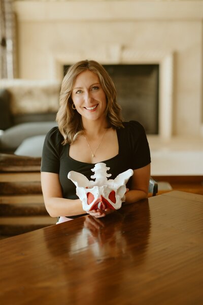 Dr Gwen hold a model of the pelvis, representing her commitment to patient education as a part of her concierge in home physical therapy services. 