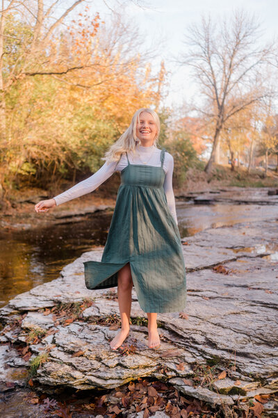Girl poses for the camera mid-twirl in a green dress near the water.