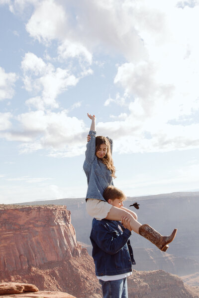 Girl on the shoulders of her boyfriend with arms in the air as they take in the breathtaking views of Dead Horse Point State Park