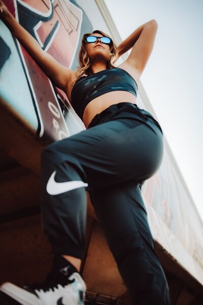 A young girl posing for her graduation photos under a mural wearing nike pants and a sports bra captured by Infinite Productions