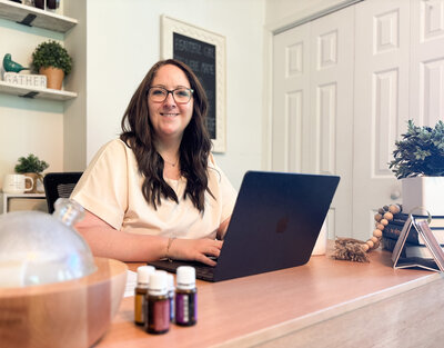 Ali smiling at camera while working on laptop in her home office for Deep Rooted Marketing