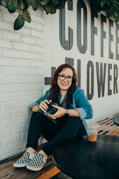 San Diego Birth Photographer sits on a bench at coffee shop with camera in hand