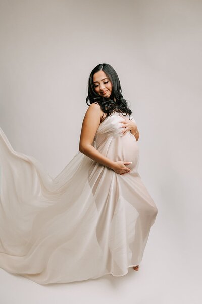 portrait of a pregnant woman covered in white silk. She is smiling and holding her belly.