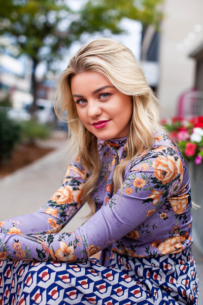 A senior portrait of a beautiful blonde girl wearing a purple floral blouse. Captured by Branson photographer Dynae Levingston