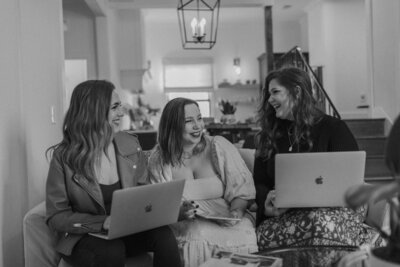 Three women sit together on a couch, each with a laptop, smiling and talking in a cozy, well-lit living room. The scene exudes a warm, collaborative vibe—perfect for friends discussing their latest white label web design course.