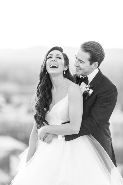 Groom embraces his bride from behind as she laughs with joy