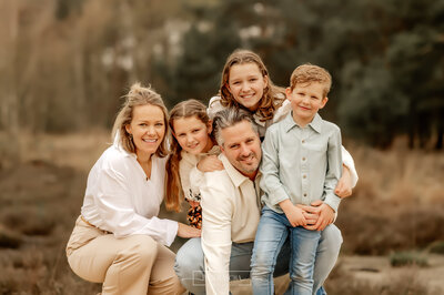 Een gezinnetje van 5 staat close bij elkaar en lachend naar de camera in het bosgebied Herperduin