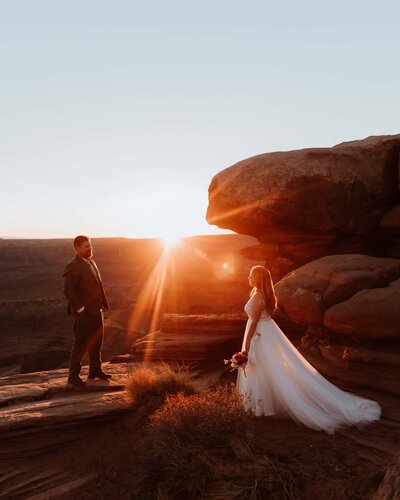 bride walks towards groom during sunset surrounded by red rocks 
