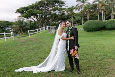 A newlywed couple casually leaning into each other as one holds the other's bouquet 