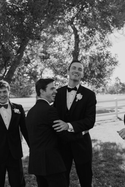 Groom and groomsmen wearing black tux hugging and laughing together during groomsmen photos.