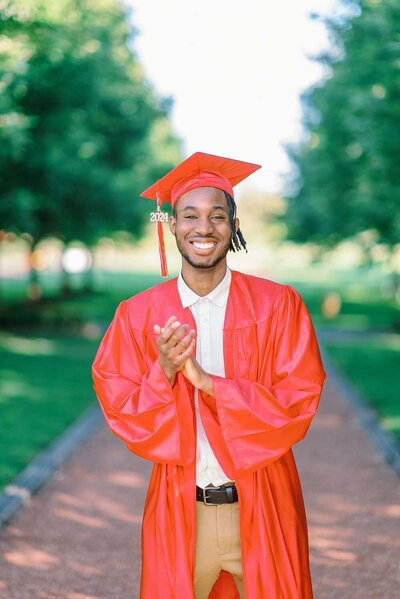 Senior guy wearing khaki pants and a white polo shirt leaning against an orange pillar