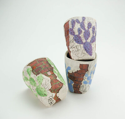 A ceramic cup that resembles plaster falling apart from red bricks with painted cacti and graffiti