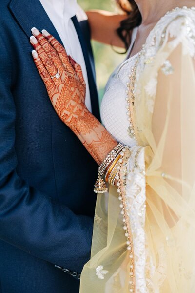 A bride with henna on her hands embraces the groom on their wedding day.
