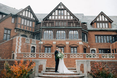 Bride and Groom stand on the staircase outside of Rollins Mansion, a  Des Moines wedding venue. Photo by one of Des Moines Iowa Wedding Photographers, Anna Brace