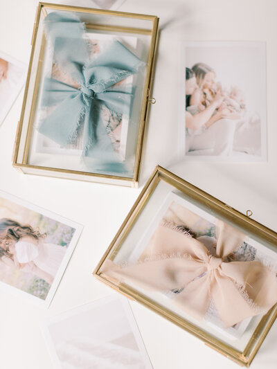 Proof prints wrapped in blue and pink ribbon  inside gold-edged  glass boxes surrounded by scattered prints