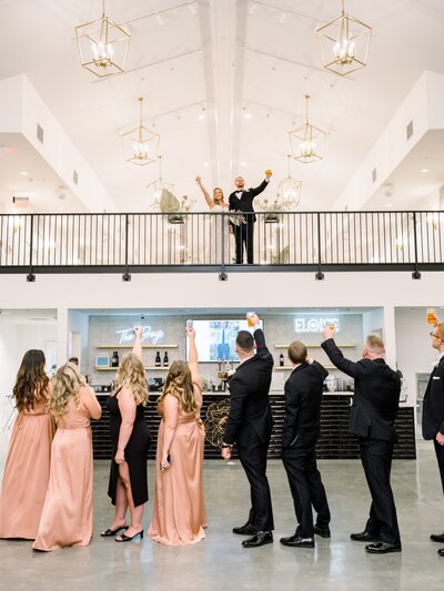 wedding party cheers to couple on balcony above  bar