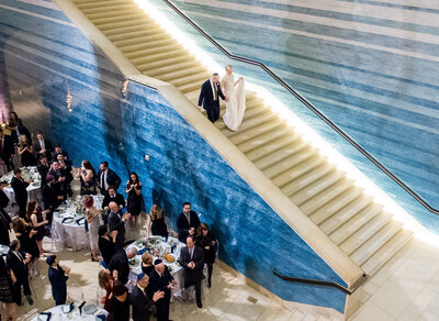 Newlyweds making a grand entrance down the stairs at Blanton Museum of Art in Austin, Texas, as guests cheer and clap in celebration.