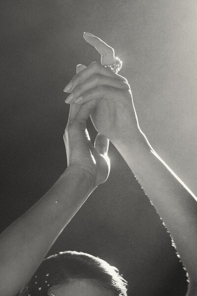 Black and white photo of woman's hands up in the air catching the glimmers of sun in a beautiful pose.