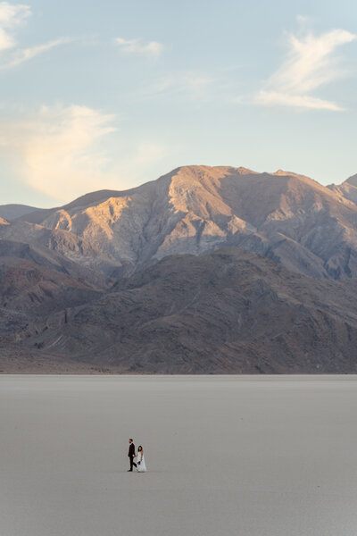A couple in wedding clothes walking on the Racetrack Playa in Death Valley National Park with mountains behind them