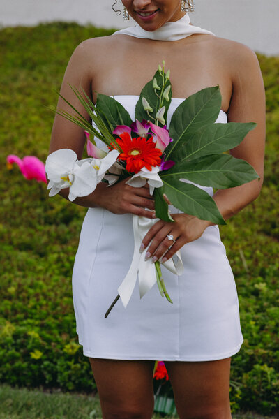 A bride holding a bouquet wearing a white dress outside