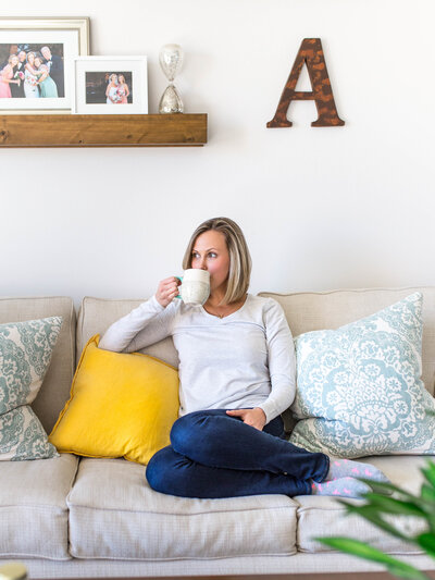 A headshot of Amanda Miller drinking a cup of coffee on the sofa.
