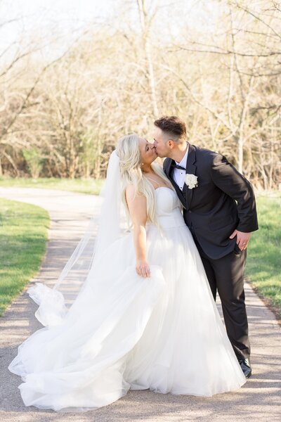 Close up of bride sitting in front of wildflowers, one hand on knees, one hand in her hair