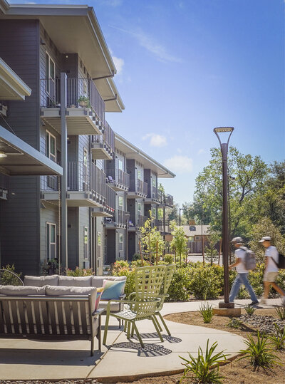 Peaceful outdoor seating at Lowden Lane Senior Apartments featuring modern architecture, landscaped pathways, and shaded gathering spaces.