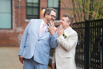 Two grooms showing off rings after getting married 
