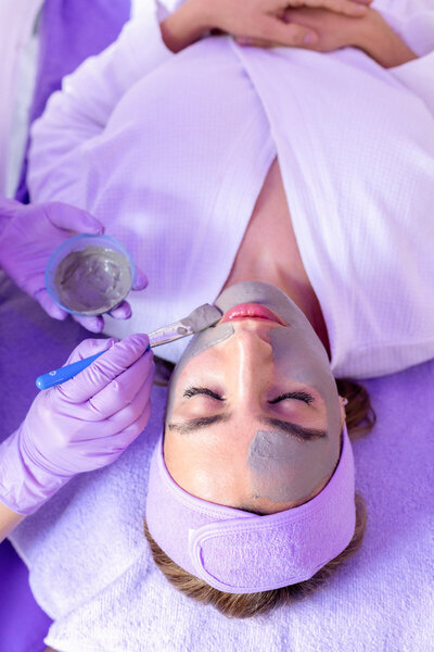 Schoonheidsspecialist die een klei masker aanbrengt op client terwijl ze poseert voor een branding fotoshoot