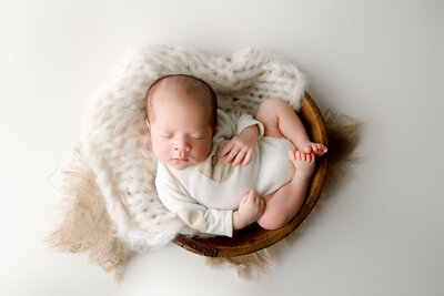 newborn baby boy wearing cream romper lying in a wood bowl, neutral, fresno california newborn photographer